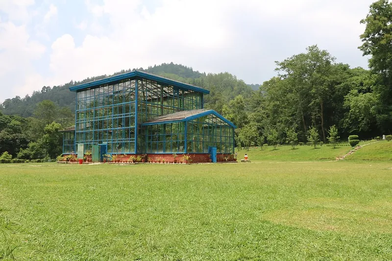 A large glasshouse on a wide lawn, with forested hills behind