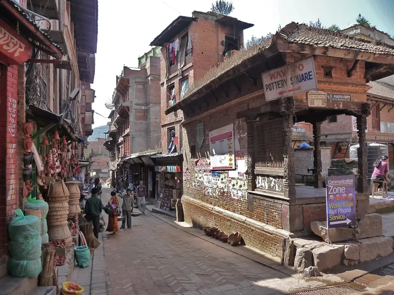 A brick lane in Bhaktapur with a sign pointing to Pottery Square and clay pots stacked outside shops