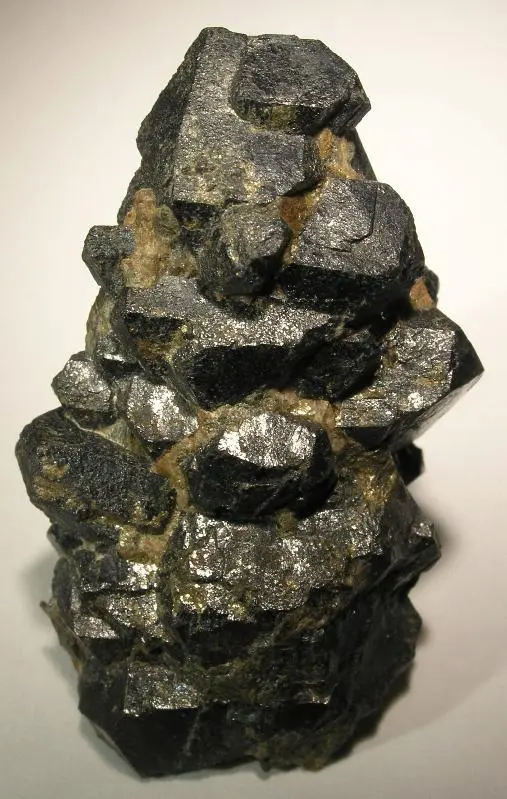 A stack of blocky, shiny black crystals with patches of pale brown mineral between them