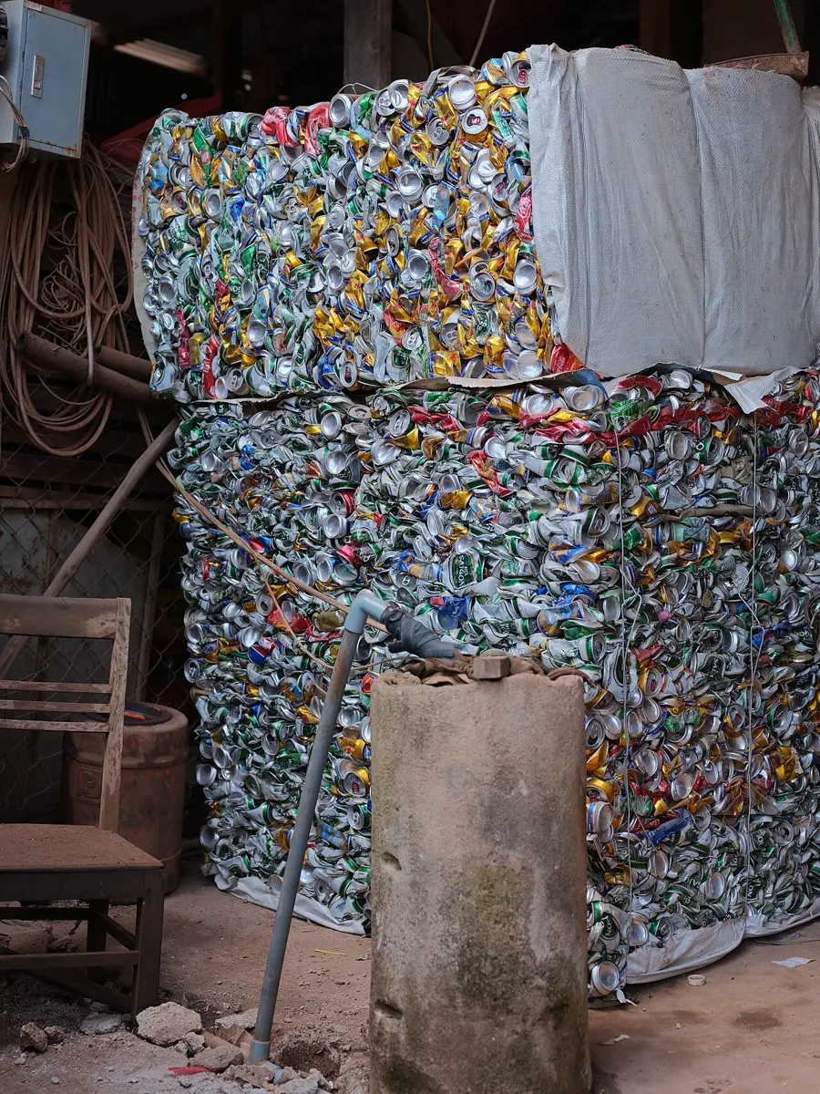 Two huge blocks of crushed, colorful drink cans, tied with wire and stacked one on top of the other in a shed