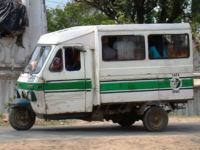 A small white three-wheeled van with green stripes and the word Safa on its side, full of passengers, on a road in Kathmandu