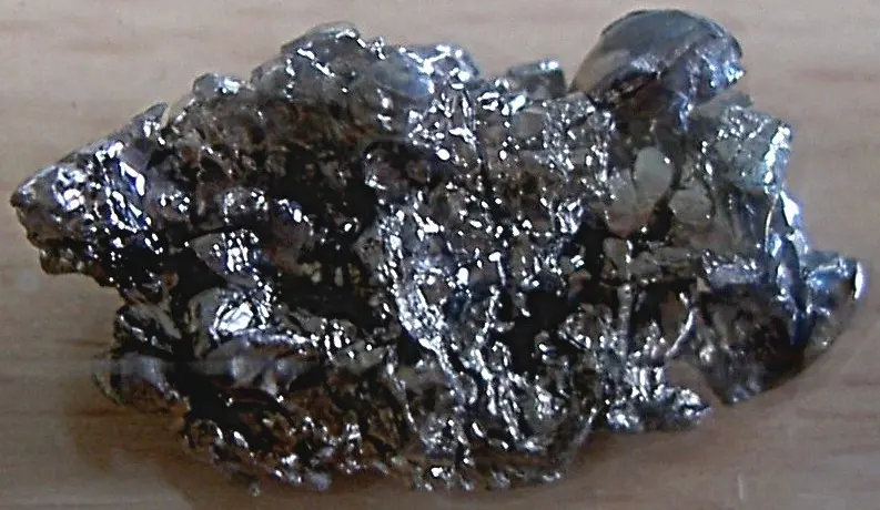 A rough, crinkled lump of shiny, dark silvery metal on a wooden surface