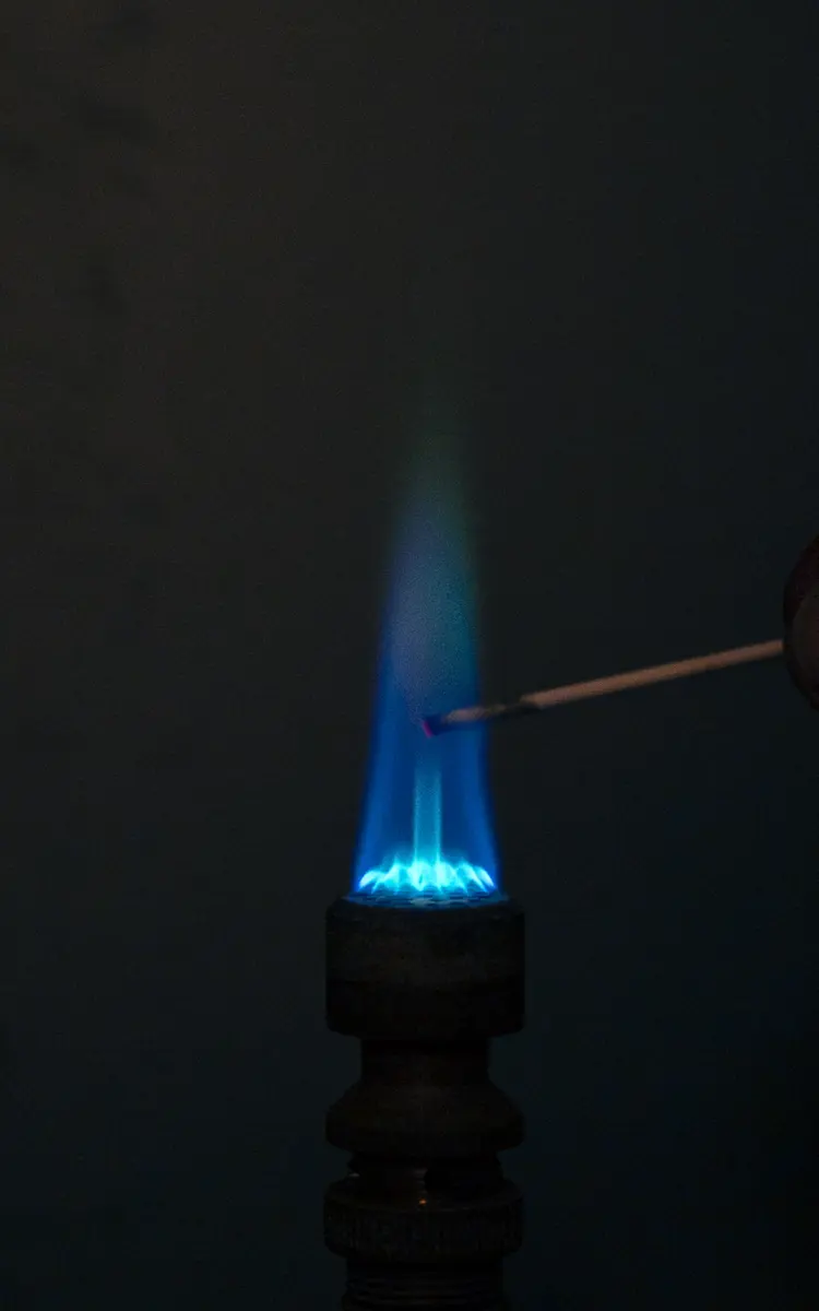 A gas flame in the dark with a thin wire held in it; the flame is mostly blue, with a faint green tinge above the wire