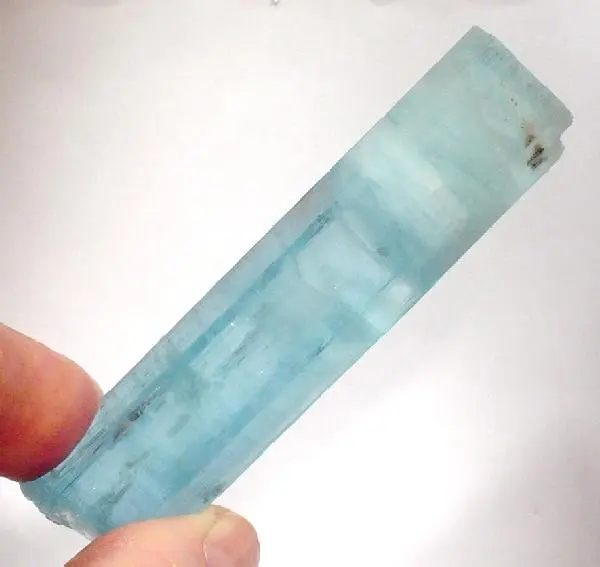 A long, clear, pale sea-blue crystal held between fingers, with a milky end and a straight, ridged side