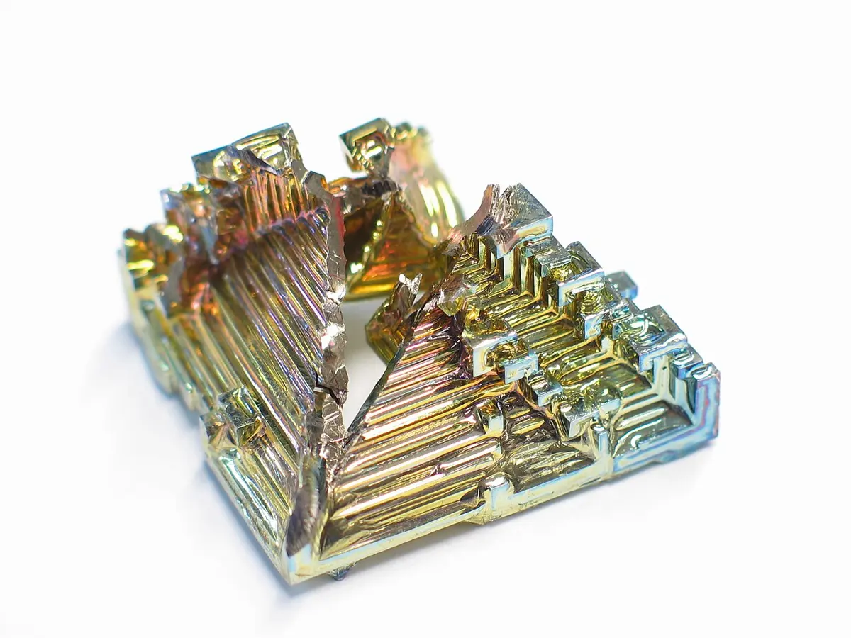 A crystal made of square steps and ridges, shining mostly gold, with patches of pink, purple, green and blue