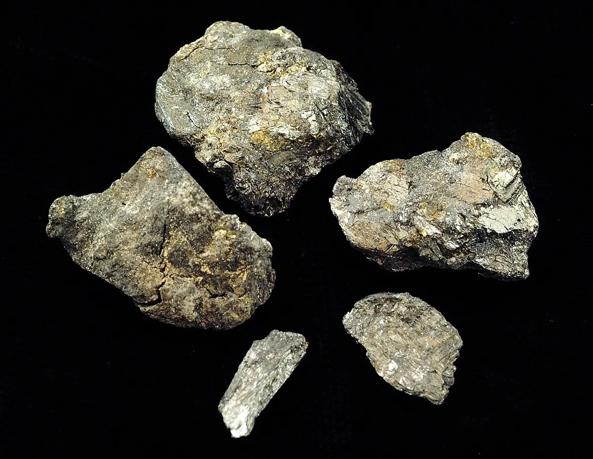 Five rough gray lumps of rock on a black background, with silvery streaks and small yellowish patches