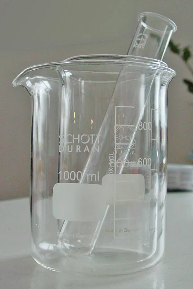 Two clear glass beakers, one inside the other, with white printed scales and the brand name Duran, and a large test tube standing in them