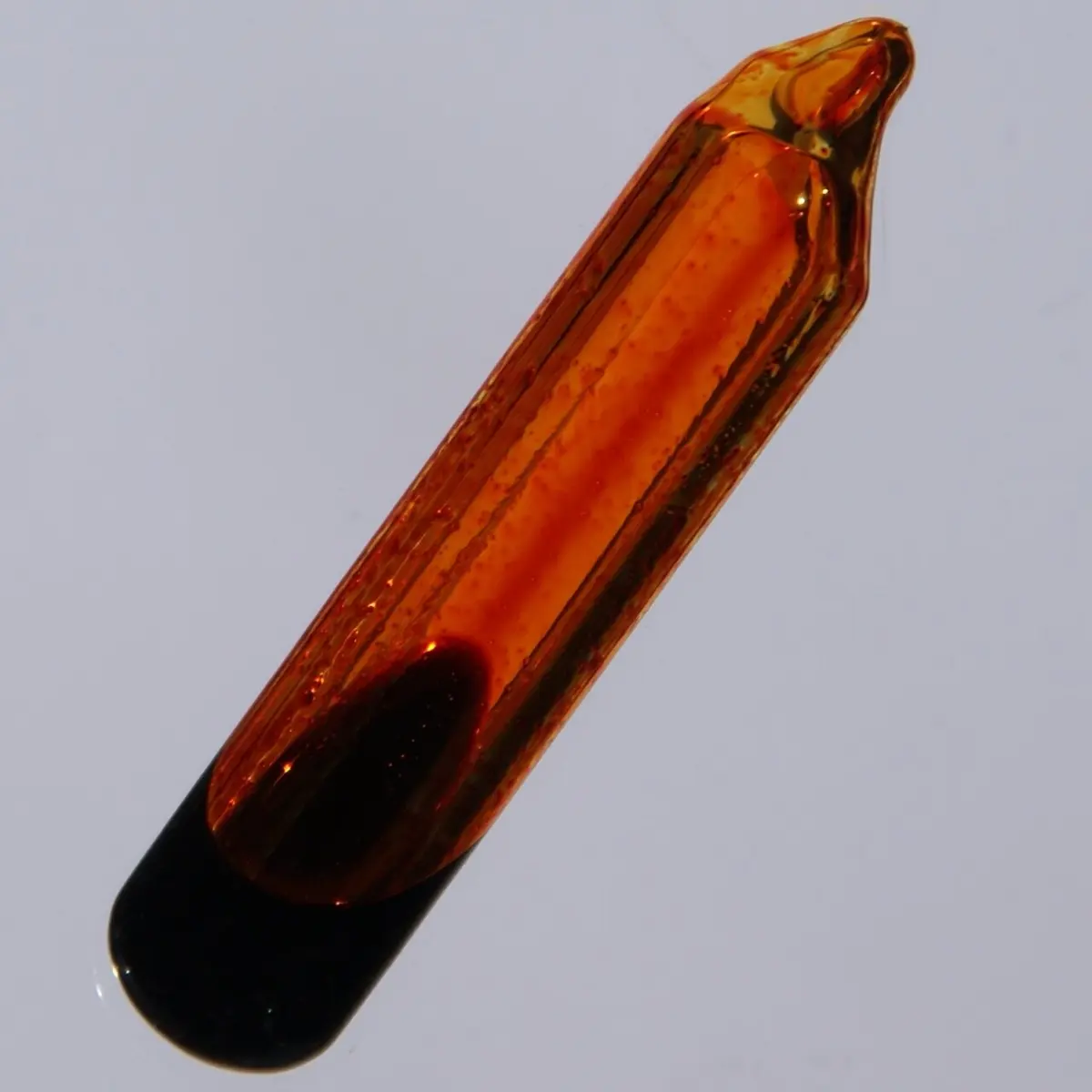 A sealed glass ampoule lying at an angle, its lower end filled with a dark red-brown liquid and the rest with clear orange vapor