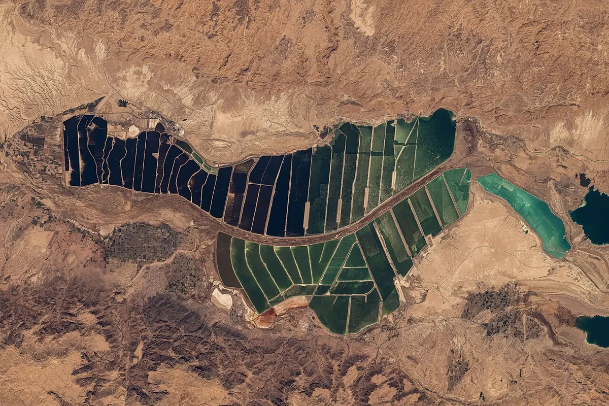 A view from space of brown desert hills around a long patchwork of straight-edged ponds, some dark blue and some deep green