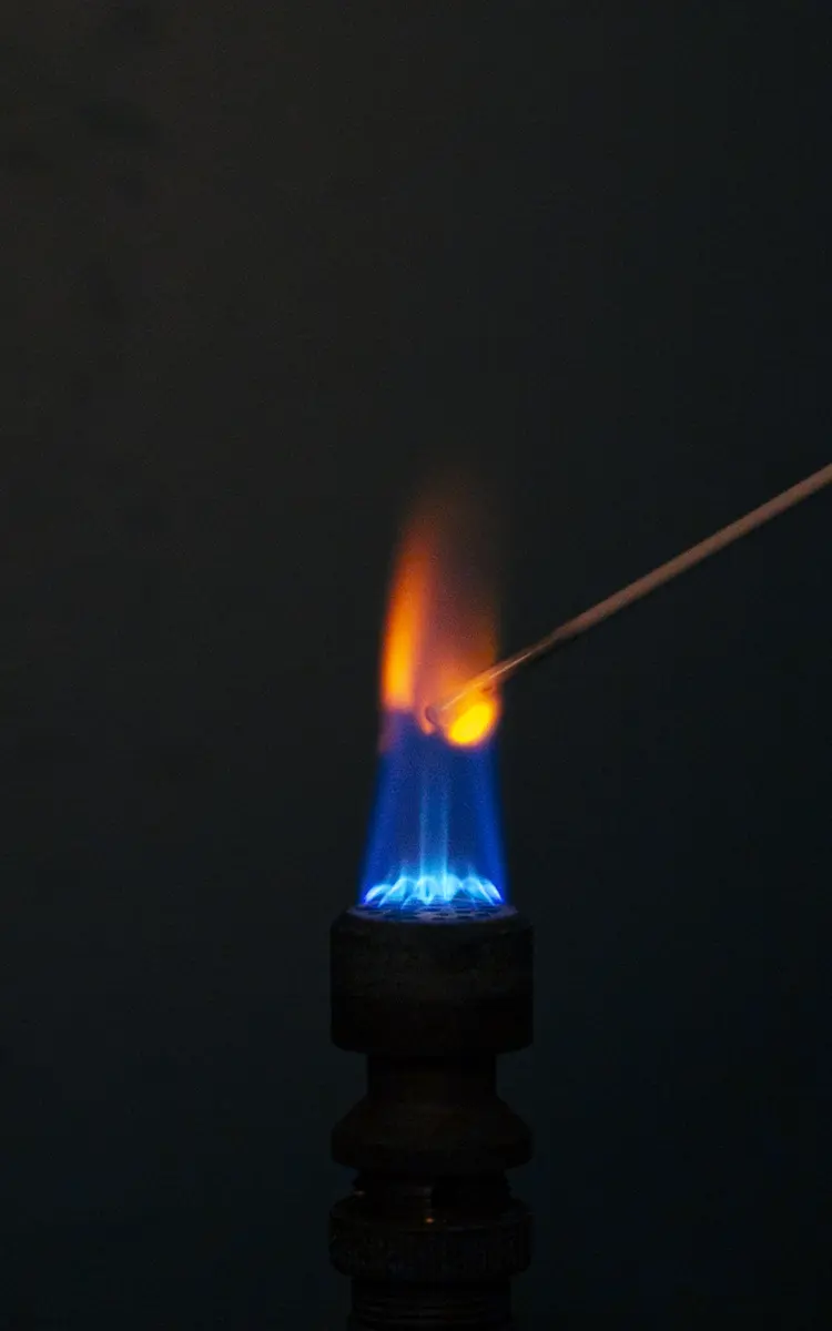 A blue gas flame in the dark with a thin wire held in it; around the wire the flame turns orange-red