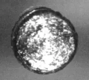 A small, round, shiny metal disc, seen from above, with a rough bright surface