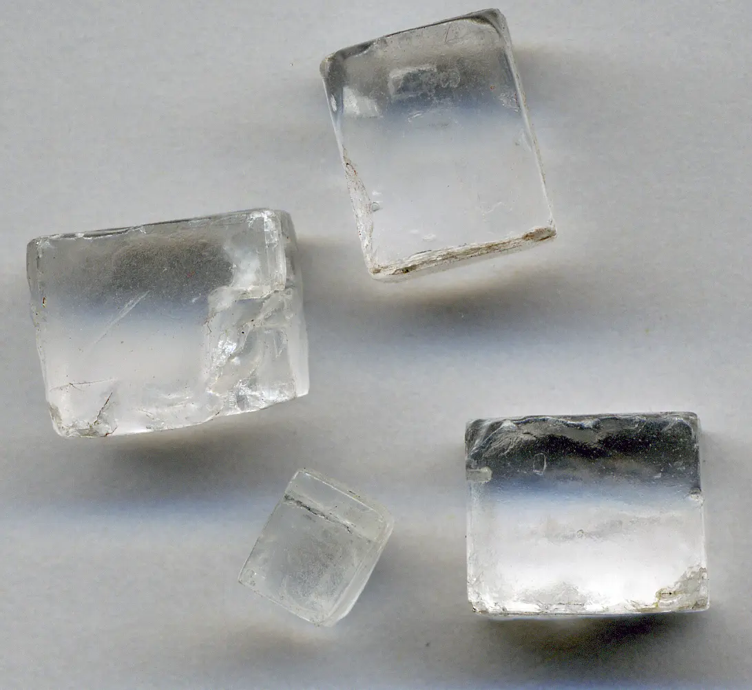 Four clear, colorless crystals shaped like small cubes and blocks, on a pale background