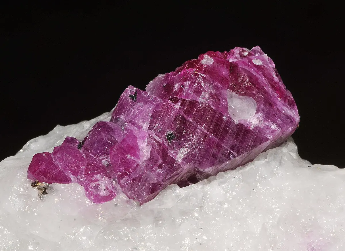 A deep pinkish-red crystal with stepped, layered sides, partly buried in white rock