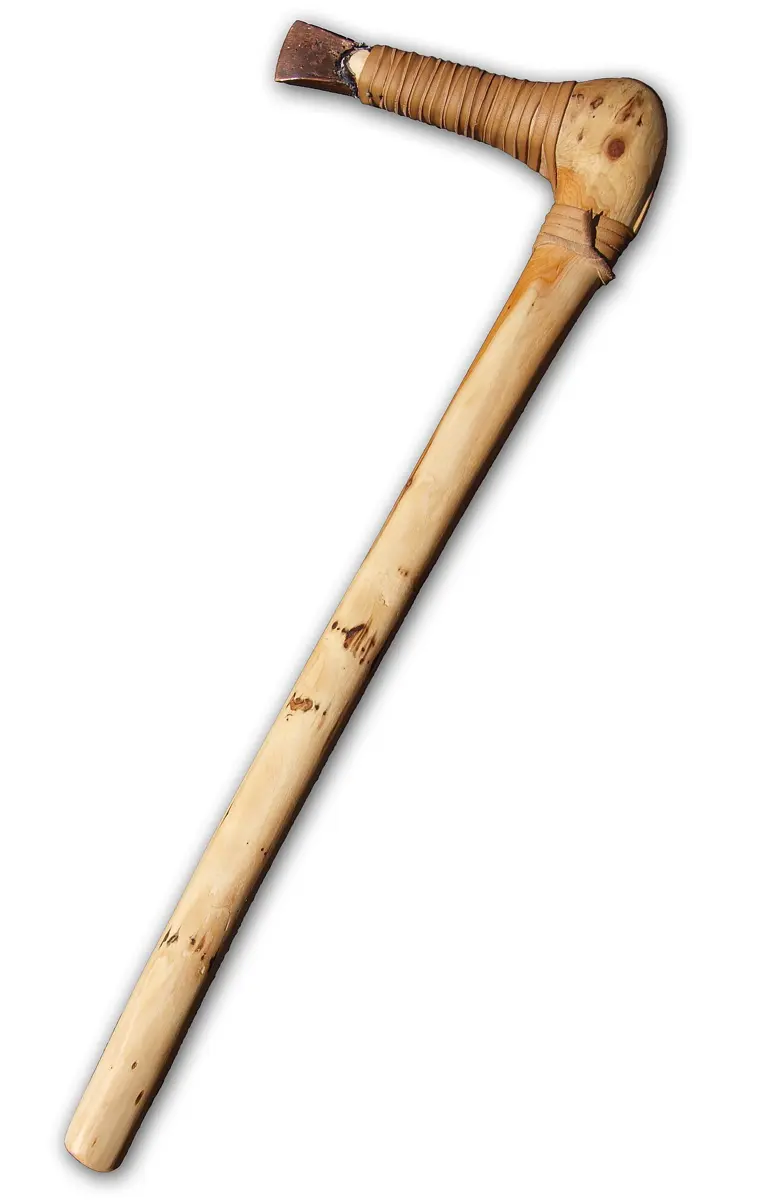 A copy of an ancient axe: a long pale wooden handle bent at the top, with a short copper blade tied into the bend with leather