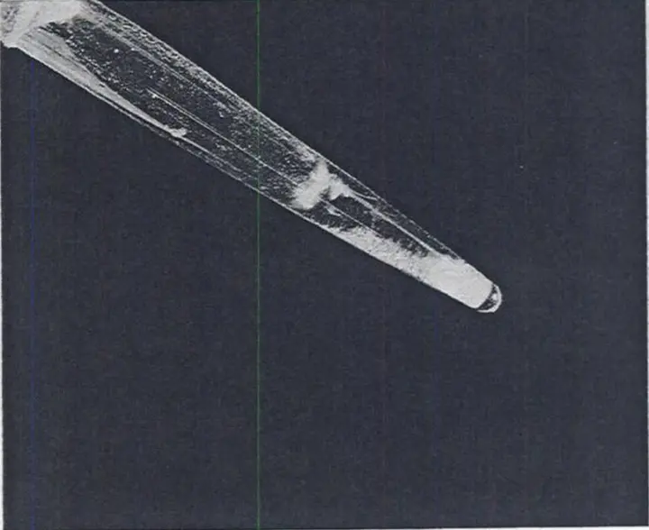 A black-and-white photo of the narrow tip of a small glass cone with a tiny pale clump of solid at its very bottom