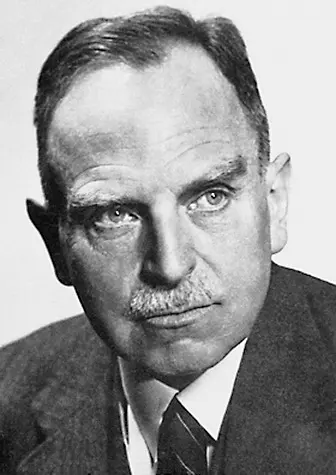A black-and-white portrait of a man with short hair and a small mustache, in a dark suit and tie, looking straight at the camera
