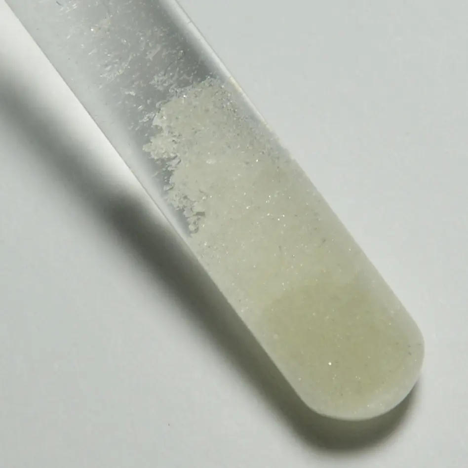 The rounded bottom of a glass test tube holding a pale yellow-green crystalline powder