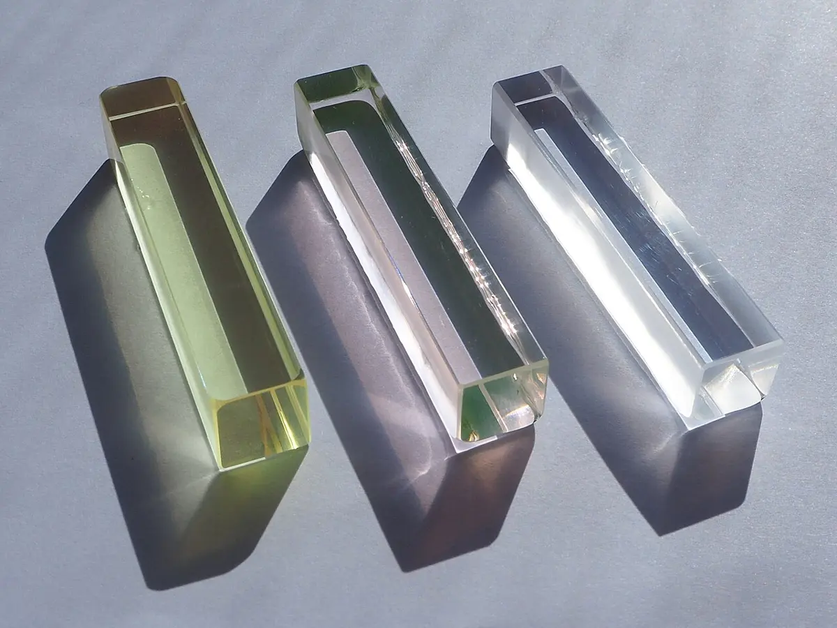 Three clear glass blocks lying side by side: the left one pale yellow-green, the middle one faintly pink, the right one colorless