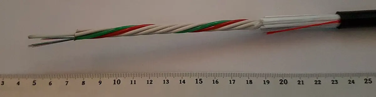 The end of a black cable, stripped back to show colored tubes with thin colored fibers inside, laid along a ruler marked in centimeters