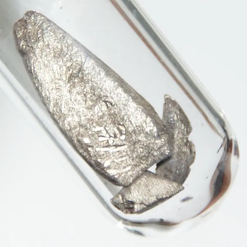 Two gray, rough pieces of metal with a slightly yellowish shine, sealed in a clear glass tube
