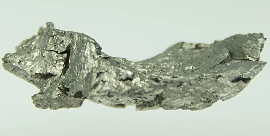 A long, rough, bright silvery piece of metal with jagged edges, on a pale background