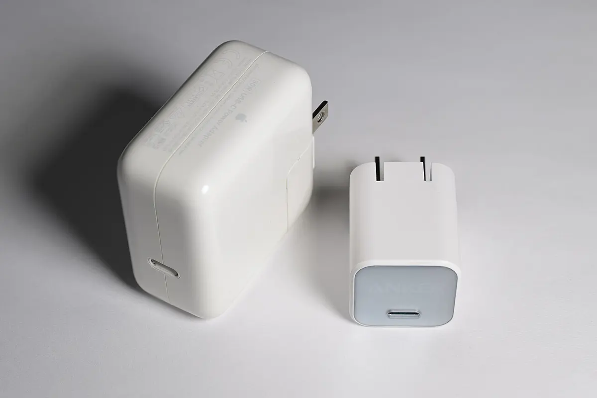Two white phone chargers side by side on a table; the one on the right is clearly smaller