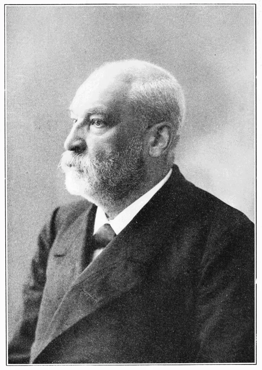 An old black-and-white portrait, in profile, of an elderly man with short white hair, a white beard and mustache, in a dark suit