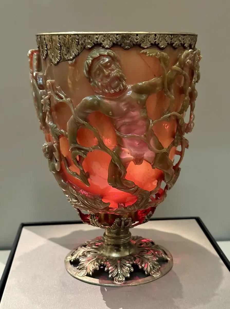 An ancient glass cup glowing ruby red, with a man tangled in vines carved in openwork on its side, in a silver-gilt rim and foot