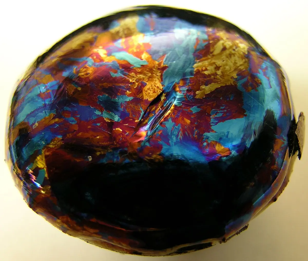 A rounded lump of metal whose whole top shimmers in patches of deep blue, purple, red and gold, with a dark band at the bottom