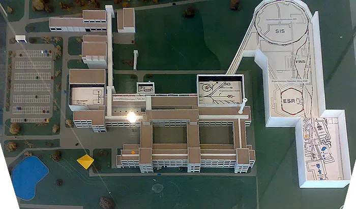 A model of a laboratory seen from above: rows of flat-roofed buildings among green lawns and, on the right, long halls with two round rooms marked SIS and ESR