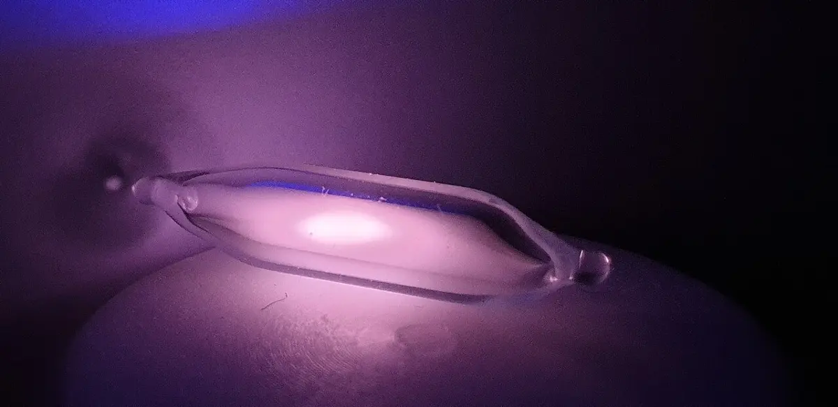 A small sealed glass capsule glowing with a soft pink-violet light in the dark