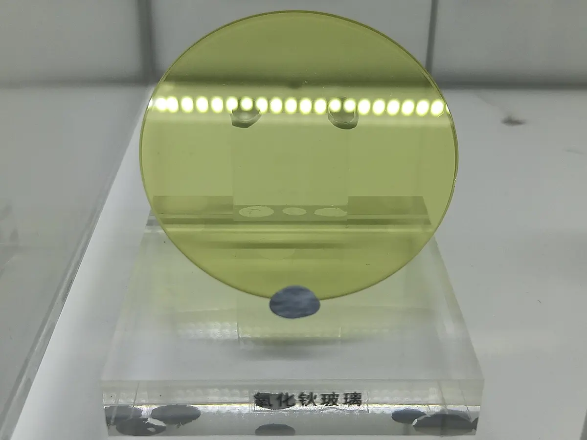 A round, yellow-green glass disc standing in a clear plastic holder, with a row of reflected lights across its top
