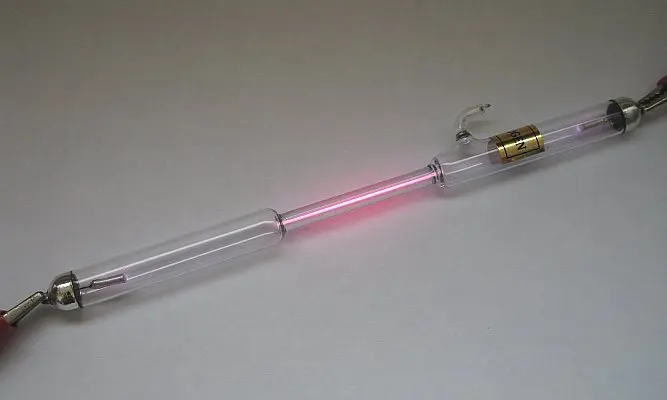 A long, thin glass tube held at both ends by metal clips, its narrow middle glowing pink
