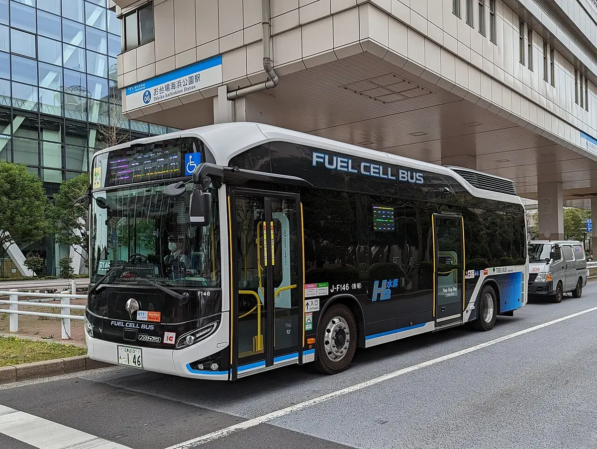 A black and white city bus with FUEL CELL BUS written on its side and an H₂ sign, parked at a station in Tokyo