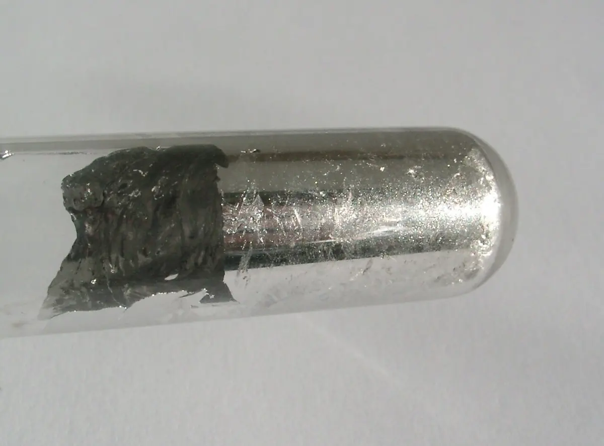 The rounded end of a glass test tube lined inside with a bright, mirror-like silver layer, with a dull gray lump of metal at its open end