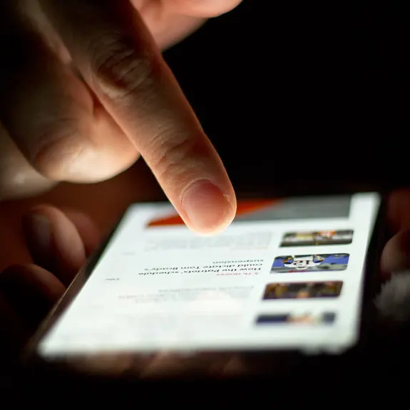 A fingertip touching the glowing screen of a smartphone in a dark room