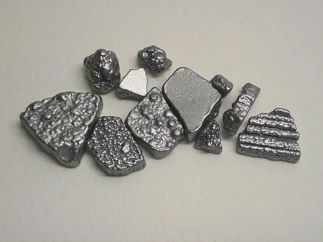 Small, flat, silvery-gray pieces of metal with rough, bumpy surfaces, on a pale gray surface