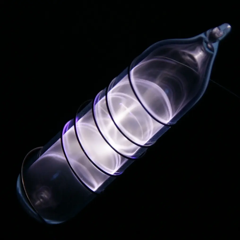 A small sealed glass vial glowing a pale whitish lilac in the dark, with a wire coiled round it