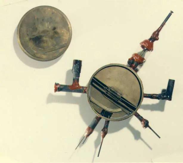 A small, round brass chamber with metal tubes sticking out on all sides, their joints sealed with red wax, lying beside its round brass lid on a white surface