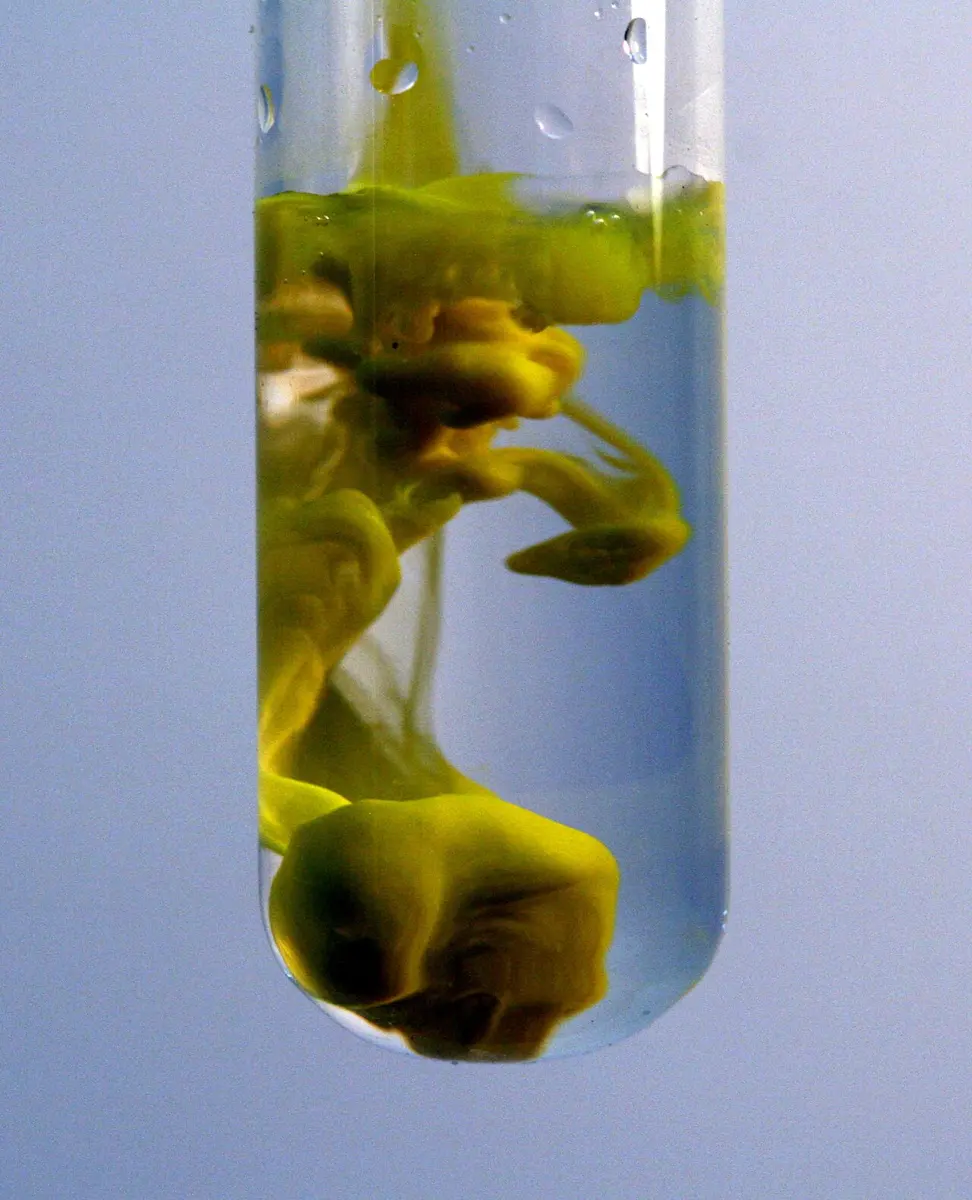 A test tube of clear liquid with swirling clouds of bright yellow solid spreading through it and settling at the bottom