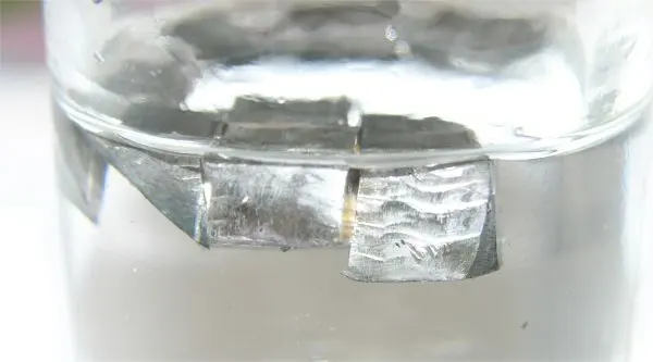 Three small silvery-gray blocks of metal floating at the top of a clear liquid in a glass
