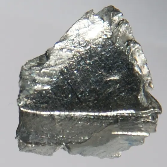 A small, flat, jagged piece of shiny silver-gray metal on a pale gray background