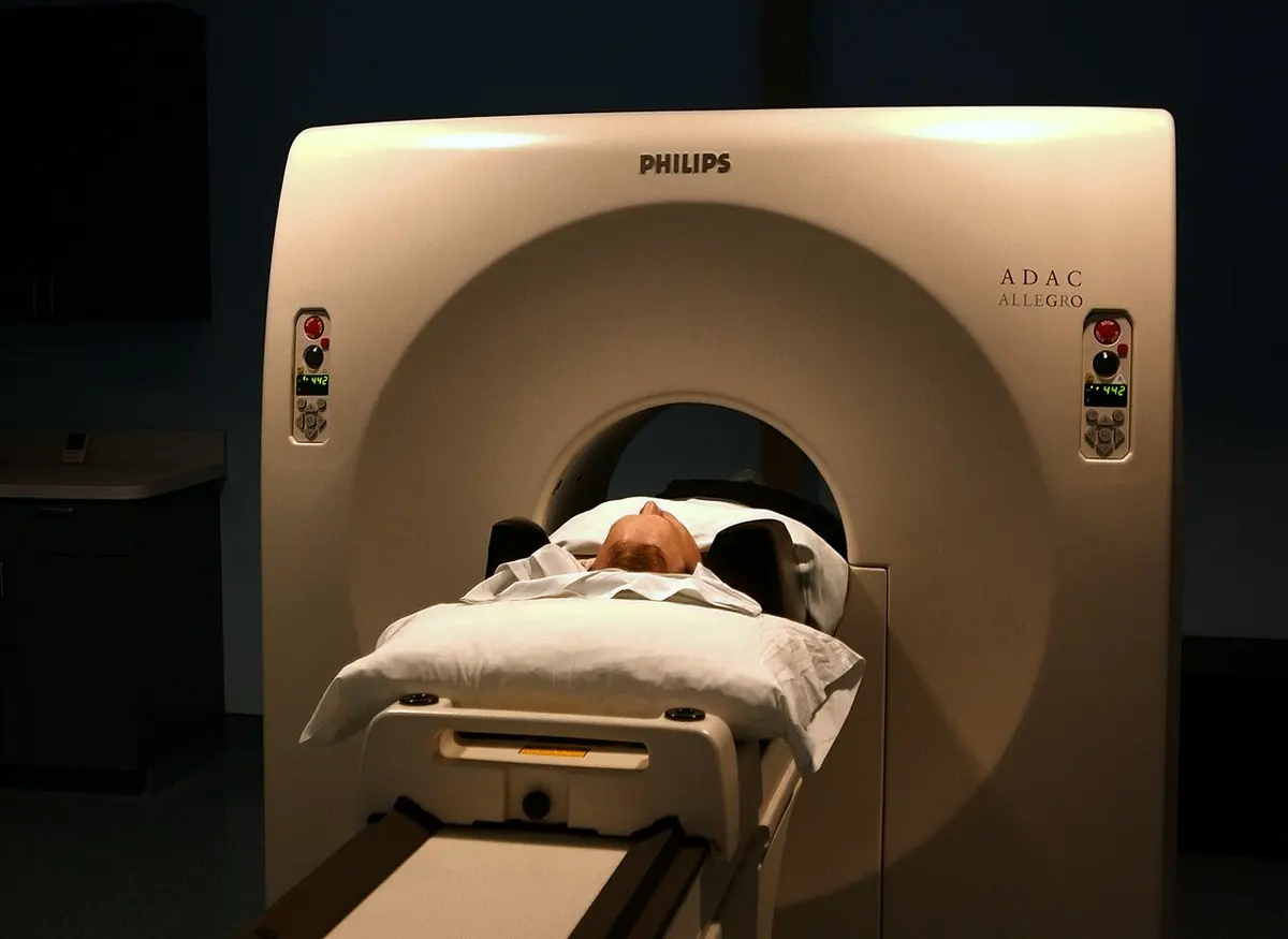 A patient lying on a padded table, head first inside the round opening of a large cream-colored scanner