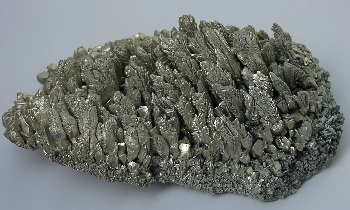 A lump covered in gray metal crystals shaped like little feathers, standing close together