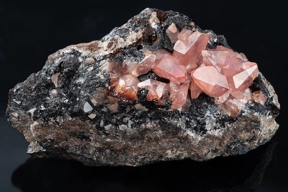 Glassy, rose-pink crystals growing on a dark, sparkly gray-black rock