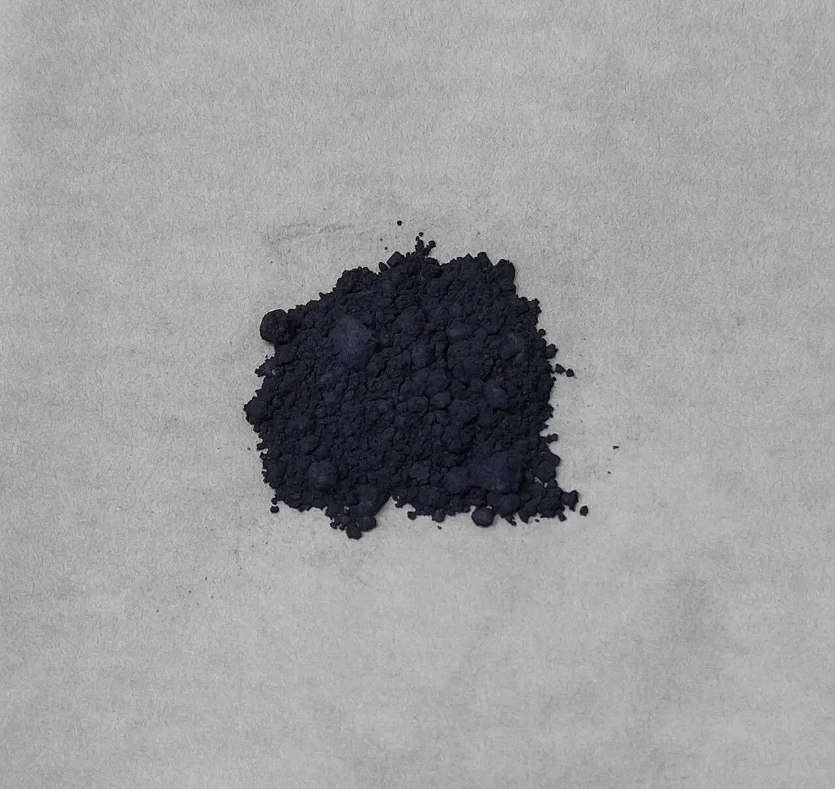 A small heap of fine, very dark blue-gray powder on a pale gray surface