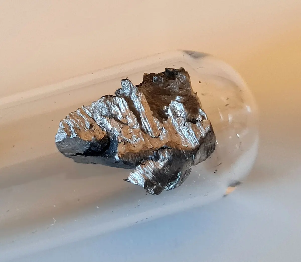 A single jagged, shiny silver-gray lump of metal inside a glass tube