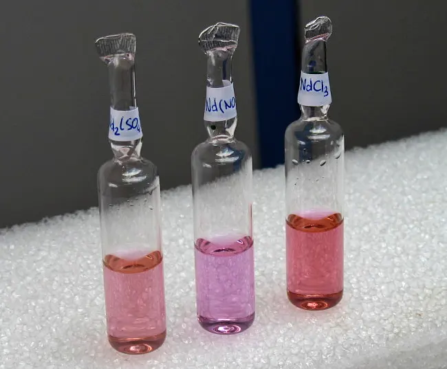 Three small sealed glass ampoules, labeled with the formulas of the salts, each holding a pink to violet-pink liquid