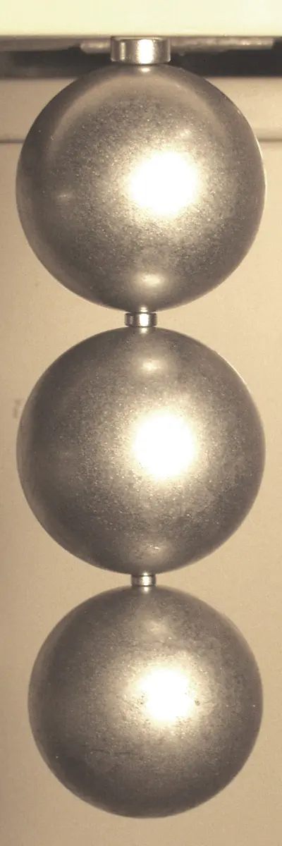 Three shiny steel balls hanging one below the other from a support at the top