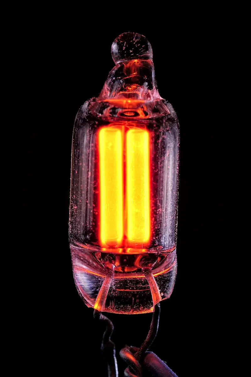 Close-up of a tiny glass bulb with two metal electrodes inside, both glowing orange